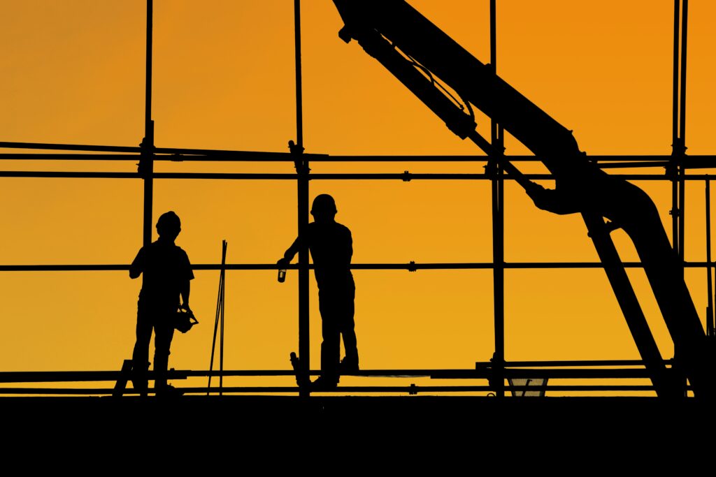 Silhouetten van twee werknemers in de bouw met zonsondergang op de achtergrond