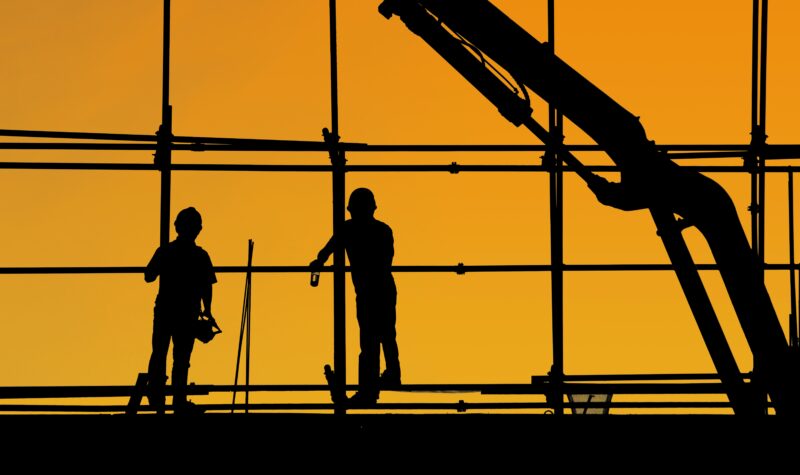 Silhouetten van twee werknemers in de bouw met zonsondergang op de achtergrond